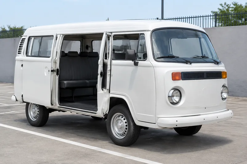 Kombi branca com as portas laterais abertas e os bancos à vista, vista de três quartos, em pátio de locadora